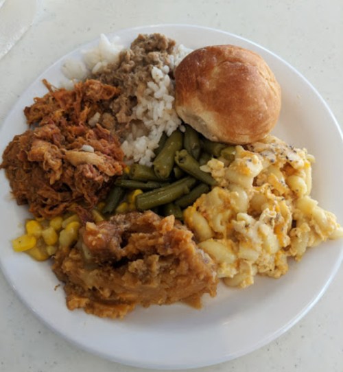 A plate of food featuring pulled pork, rice, green beans, macaroni and cheese, corn, and a roll.