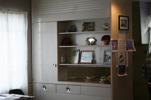 A vintage-style cabinet with shelves displaying framed photos, decorative items, and a bowl of fruit.