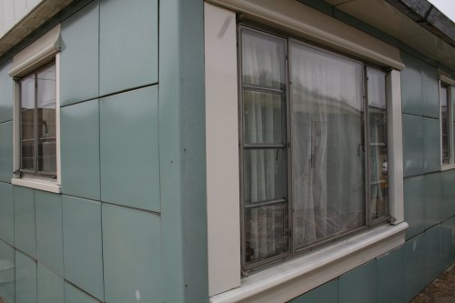 A corner view of a building with teal paneling and a window featuring multiple panes.