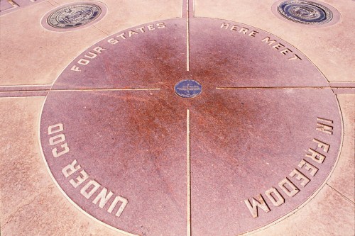 A circular stone marker with inscriptions celebrating the meeting point of four states, featuring symbols and text.