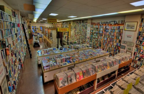 A spacious bookstore filled with shelves of books and magazines, featuring a sign for the basement entrance.