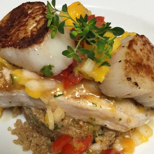 Grilled fish topped with seared scallops, mango salsa, and fresh herbs, served on a bed of quinoa and diced vegetables.
