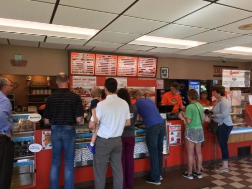 A busy ice cream shop with customers at the counter looking at the menu and ordering ice cream.