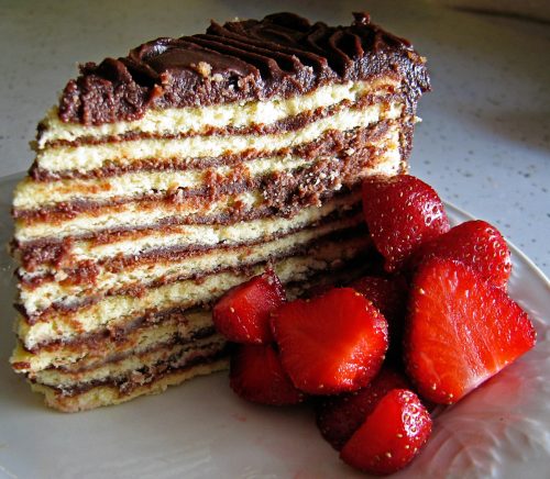 A slice of layered chocolate cake with rich frosting, served with fresh strawberries on the side.