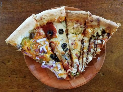 A wooden plate with five slices of pizza, each topped with different ingredients like pepperoni, olives, and onions.