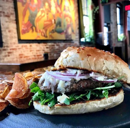A juicy burger with lettuce, onions, and sauce, served with crispy potato chips on a black plate in a cozy restaurant.