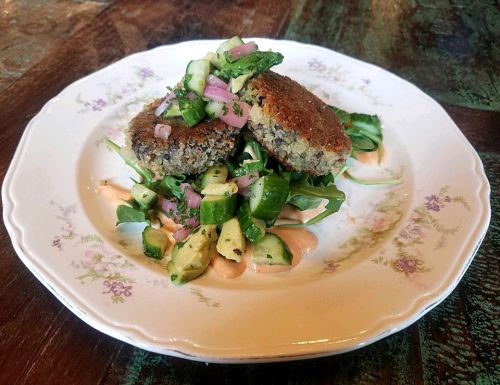 A plate with two crispy patties topped with fresh cucumber and onion salsa, served on a bed of greens with sauce.