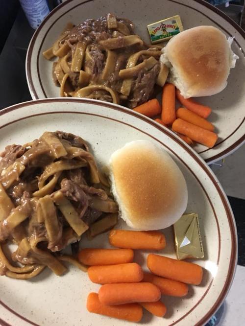 Two plates of beef and noodles with carrots and dinner rolls, served with butter and a small dessert.