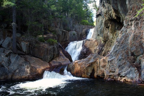 A serene waterfall cascading over rocky cliffs into a calm pool, surrounded by lush trees and natural scenery.