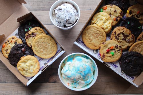 Two boxes of assorted cookies and a bowl of ice cream on a wooden surface.