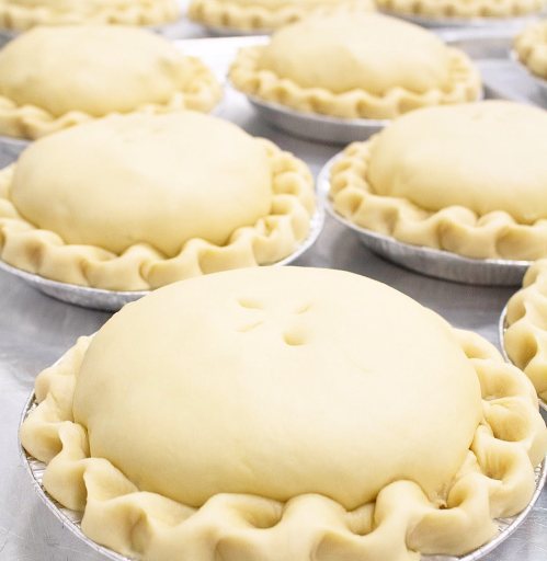 Several unbaked pie crusts in aluminum tins, each with a crimped edge and a small cut on top.