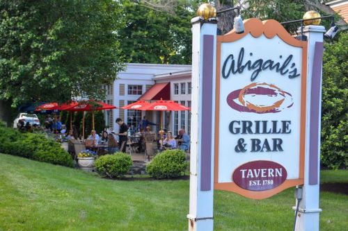 Sign for Abigail's Grille & Bar with outdoor seating and umbrellas, surrounded by greenery.