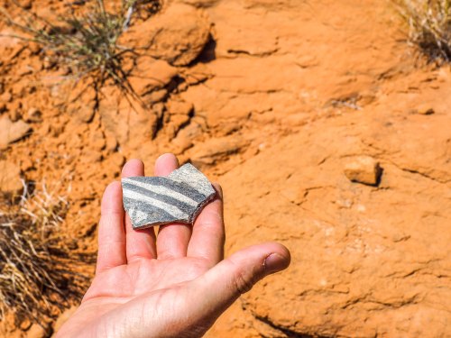 A hand holding a striped rock against a backdrop of orange rocky terrain.