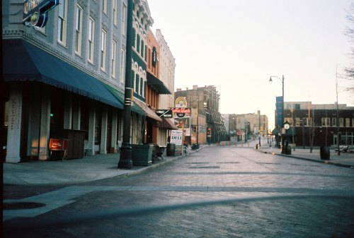 Quiet street scene at dawn, featuring historic buildings and storefronts, with empty sidewalks and soft morning light.