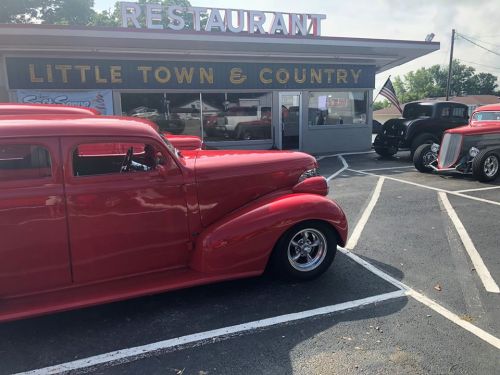 A red classic car parked in front of the Little Town & Country restaurant, with additional vintage cars nearby.