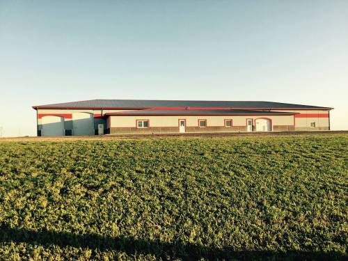 A large, modern building with a red roof and trim, set against a clear sky and green grass.