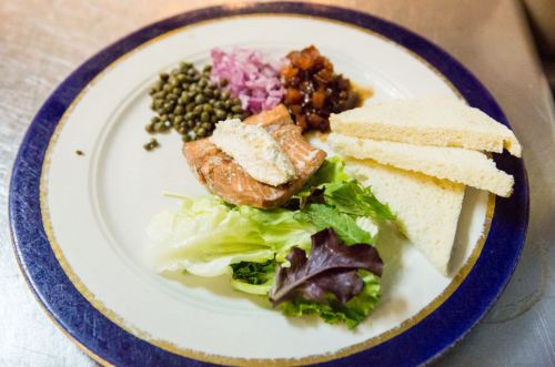 A plate with salmon, lentils, pickled onions, chutney, lettuce, and slices of white bread.