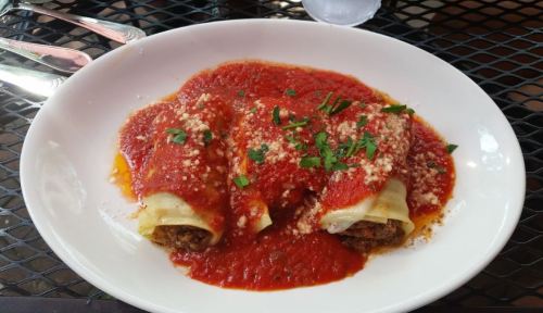 Three stuffed cannelloni topped with marinara sauce, grated cheese, and fresh parsley on a white plate.