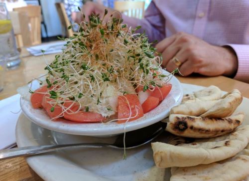 A bowl of salad topped with sprouts and tomatoes, served with warm flatbread on the side.