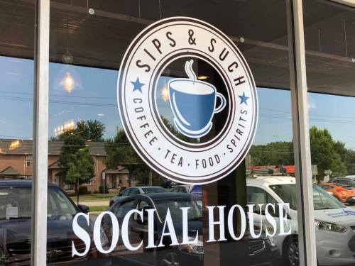 Logo on a storefront window for "Sips & Such," featuring coffee, tea, food, and spirits, with "Social House" below.