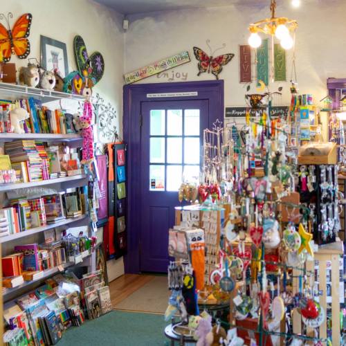 A colorful shop interior filled with books, toys, and decorative items, featuring a purple door and vibrant wall art.