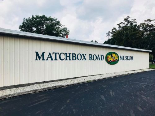 Exterior of the Matchbox Road Museum building with a colorful sign and a gravel path in front.