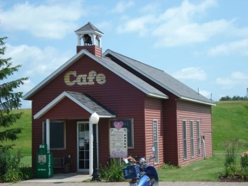 A charming red cafe building with a bell tower, surrounded by greenery and a blue sky with fluffy clouds.