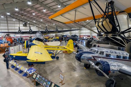 A spacious aircraft museum featuring various vintage planes, including a yellow biplane and a silver passenger aircraft.