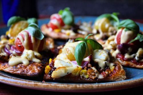 A close-up of delicious pizza slices topped with fresh basil, tomatoes, and a creamy sauce on a decorative plate.