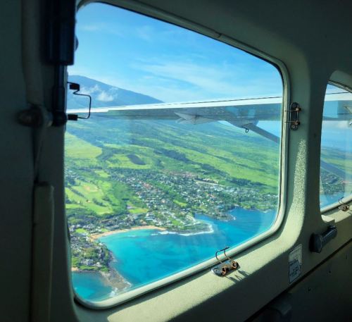 View from an airplane window showing lush green landscapes and turquoise waters below.
