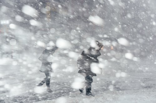 Two figures walk through a heavy snowstorm, with snowflakes swirling around and visibility greatly reduced.