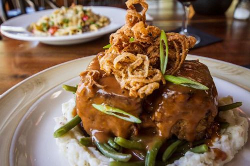 A plate of meatloaf topped with crispy onions and green onions, served on a bed of mashed potatoes and green beans.