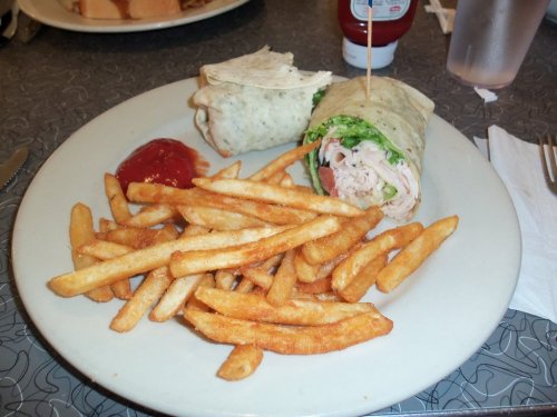 A plate with a wrap filled with lettuce and turkey, served with a side of crispy French fries and ketchup.