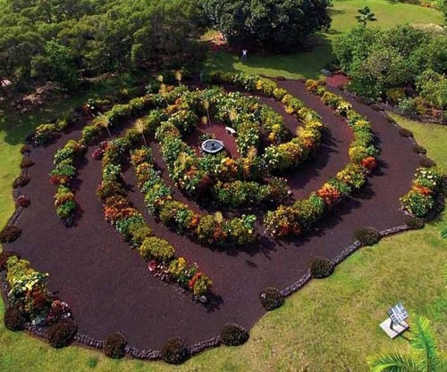 Aerial view of a spiral garden maze filled with colorful flowers and greenery, surrounded by a grassy landscape.