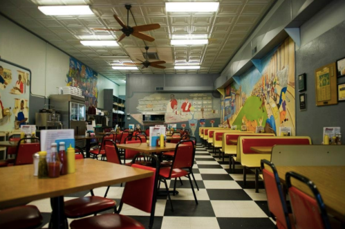 A colorful diner interior with checkered floors, empty tables, and vibrant murals on the walls.