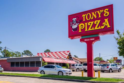 Sign for Tony's Pizza, established in 1968, with a red and yellow design and a checkered roof on a sunny day.