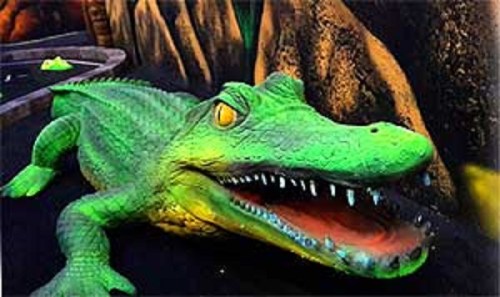 A large, green crocodile sculpture with an open mouth, set against a rocky background.