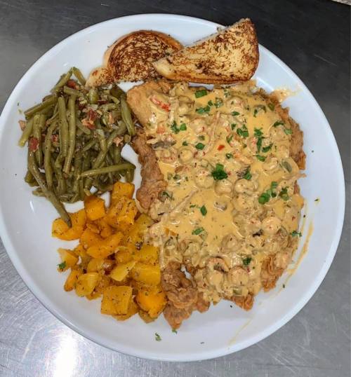 A plate featuring fried chicken topped with creamy sauce, green beans, roasted squash, and a slice of toasted bread.