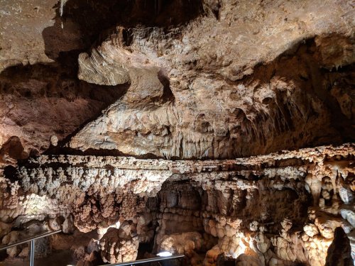A dimly lit cave interior featuring intricate rock formations and stalactites hanging from the ceiling.