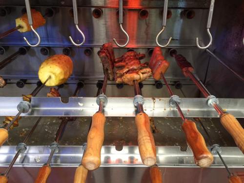 Skewers of grilled meats and vegetables on a rotisserie, with wooden handles and a shiny metal background.