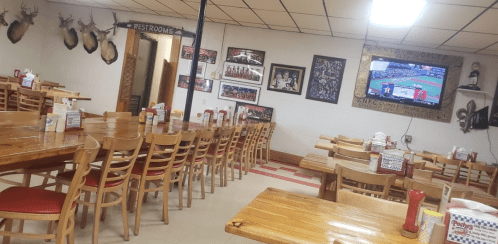 A spacious restaurant interior with wooden tables, chairs, and a TV showing a sports game on the wall.
