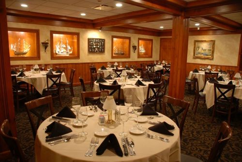 Elegant restaurant interior with wooden accents, neatly set tables, and nautical-themed artwork on the walls.