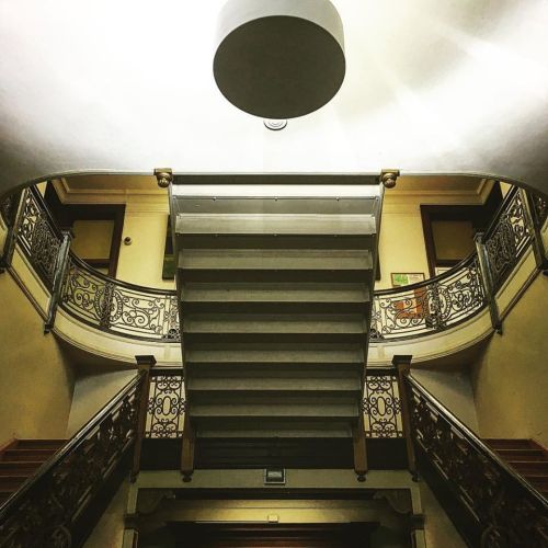 A view of a grand staircase with ornate railings, illuminated by a central ceiling light.