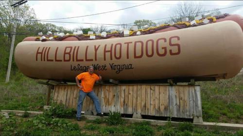 A person poses next to a giant hot dog sign for "Hillbilly Hotdogs" in LeSage, West Virginia.