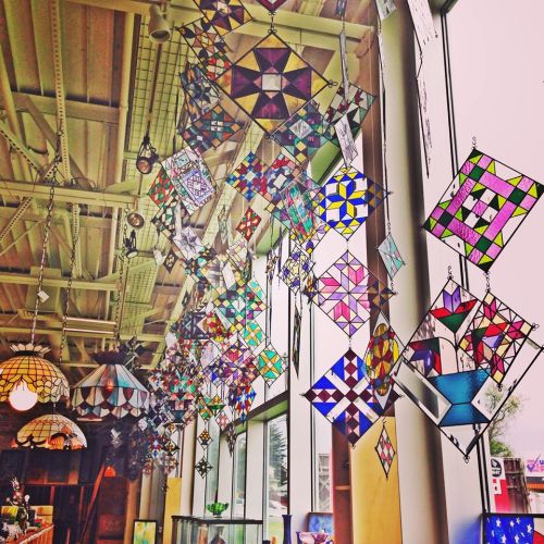 Colorful stained glass hangings suspended from the ceiling, casting vibrant light in a bright, airy space.