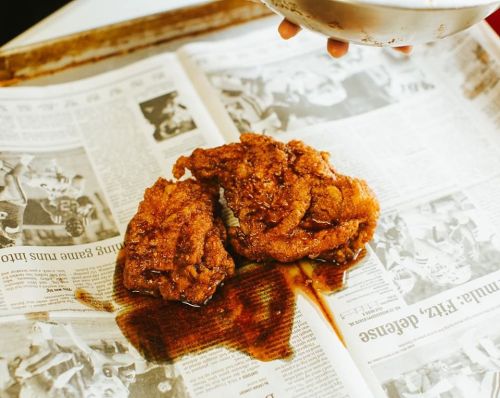 Two pieces of fried chicken on newspaper, with a drizzle of sauce pooling around them.