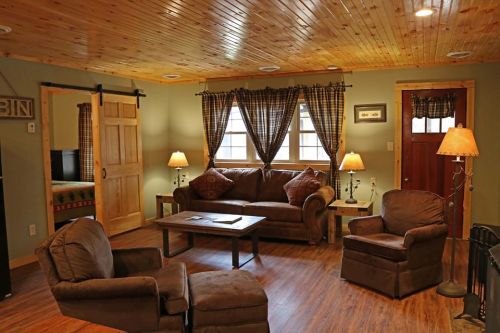 Cozy living room with wooden ceiling, brown furniture, warm lighting, and patterned curtains.