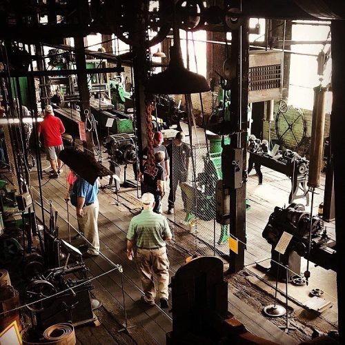 A vintage workshop filled with machinery and visitors exploring the industrial space.