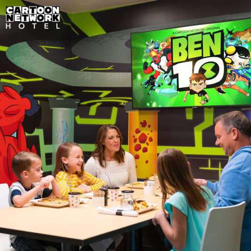 A family enjoys a meal in a Cartoon Network-themed room featuring a Ben 10 screen and colorful wall graphics.