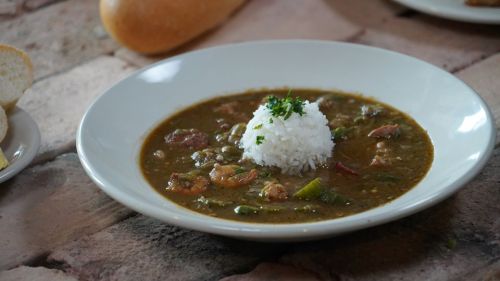 A bowl of green gumbo with shrimp and meat, topped with a mound of white rice and garnished with parsley.